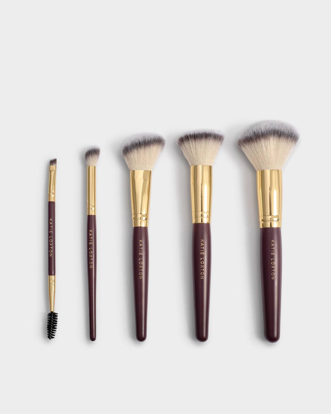 Set of makeup brushes with brown handles and gold accents on a light gray background